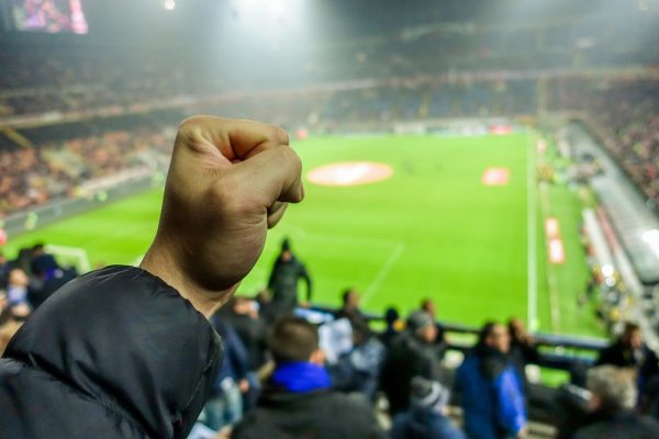 Soccer fan celebrate their team in football italian stadium - Hooligans people watching sport match - Love for sport concept - Focus on man close hand - Warm filter with original stadium lights