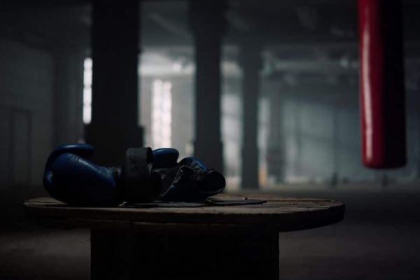 Box sport concept. Closeup boxing gloves lying on wooden box in empty gym. Fitness equipment in sport club. Modern gym with punching bag for boxing training on background.